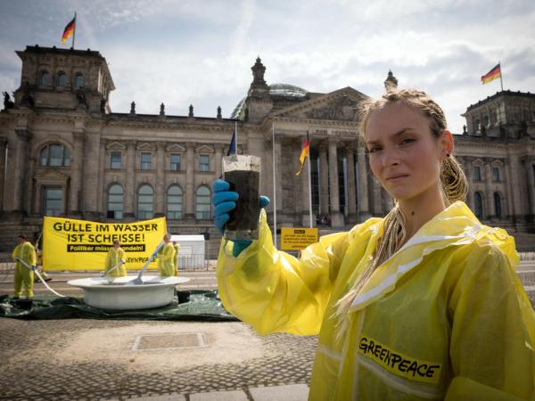 Drei Meter großen Teller voller Gülle vor dem Reichstag in Berlin: Eine Aktivistin hält einen Becher mit dunkler Flüssigkeit. Auf dem Banner steht: „Gülle im Wasser ist Scheiße! Politiker müssen handeln.“