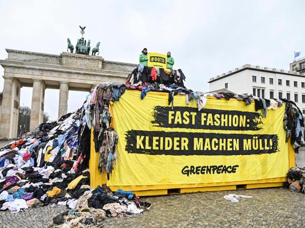 Aktive sitzen auf einem einem 3,5 Meter hohen und 12 Meter breiten Textilmüll-Berg  vor dem Brandenburger Tor, auf dem Banner steht "Fast Fashion: Kleider machen Müll".