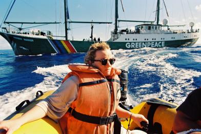 August 1995: Protest gegen die Wiederaufnahme französischer Atomwaffentests auf Moruroa. Ein Greenpeace-Aktivist auf einem Schlauchboot.  Im Hintergrund Das Greenpeace-Flaggschiff RAINBOW WARRIOR auf dem Weg nach Moruroa. 