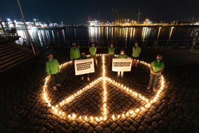 Peacezeichen aus Kerzen im Dunkeln, darin gegen Atomwaffen protestierende Greenpeace-Aktive