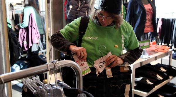 Eine Aktivistin versieht in einem Geschäft Kleidung mit dem Etikett "Diese Textilie hat Wasserverschmutzung verursacht".