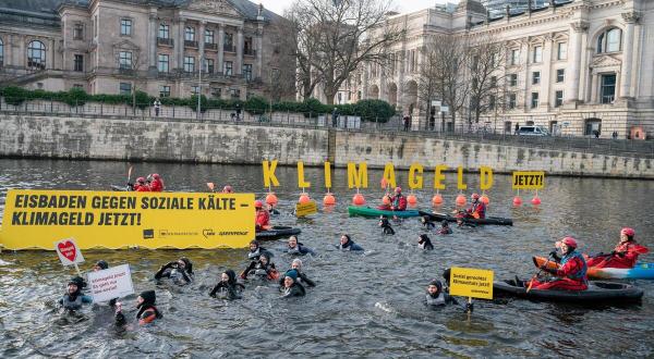 Aktive in Booten und im Wasser der Spree, große Buchstaben auf Schwimmbojen bilden den Schriftzug „Klimageld jetzt!“